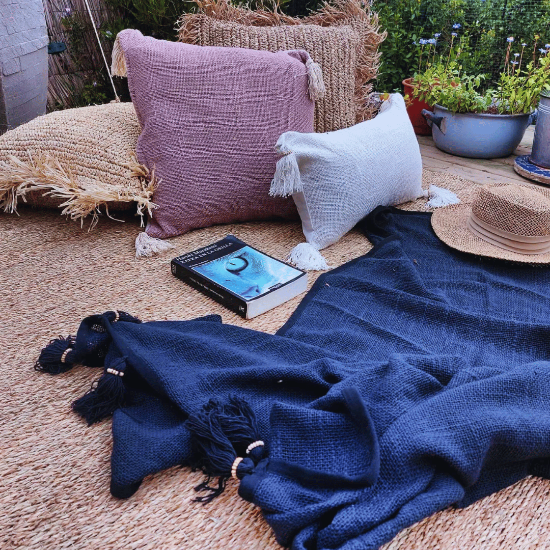 Terraza armada con una alfombra, cojines, mantas y libro, para disfrutar afuera