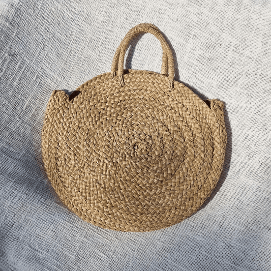 Cartera Seminyak redonda de rafia natural estilo boho para verano, fondo manta medan blanca