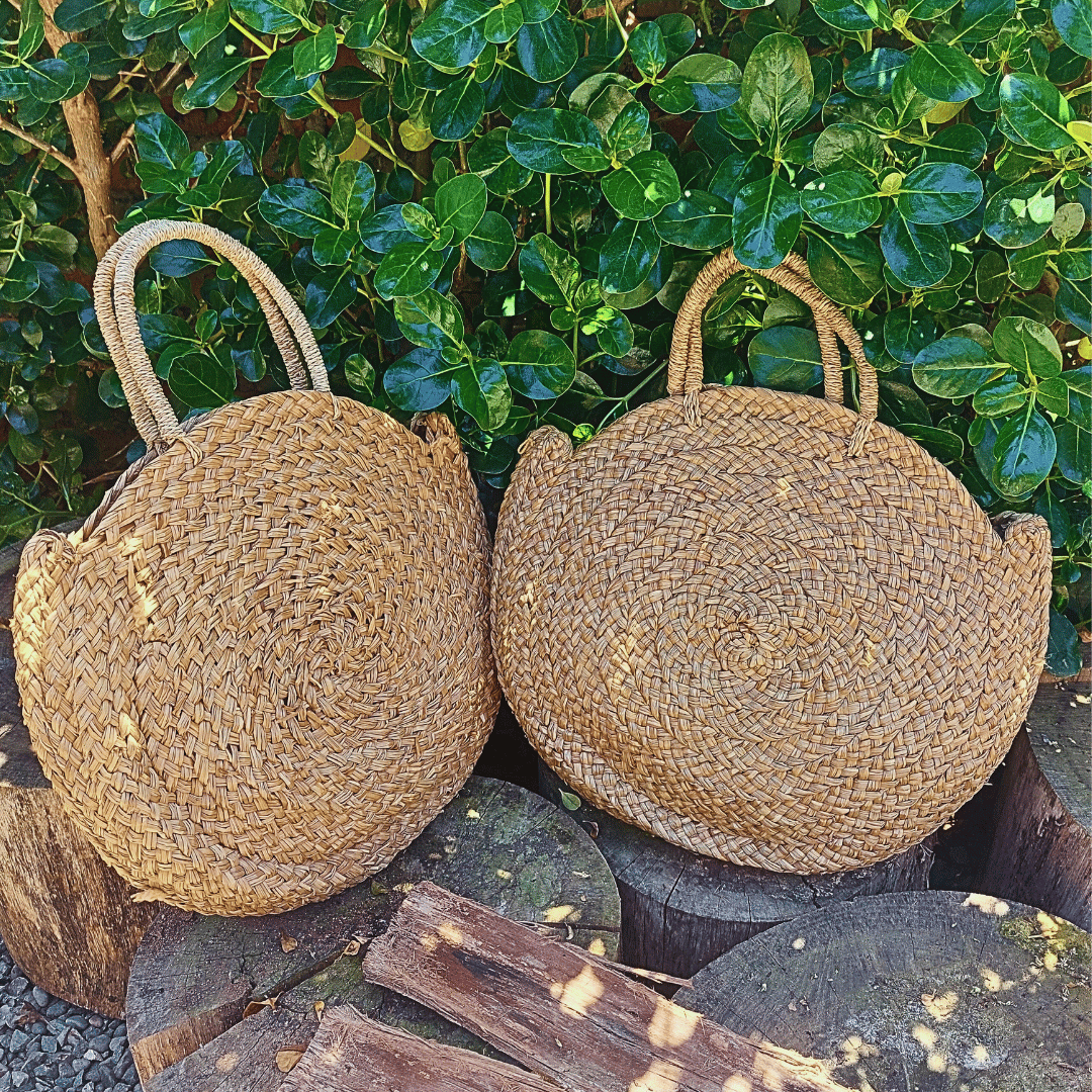 Carteras Seminyak redondas de rafia natural estilo boho para verano, con fondo de plantas