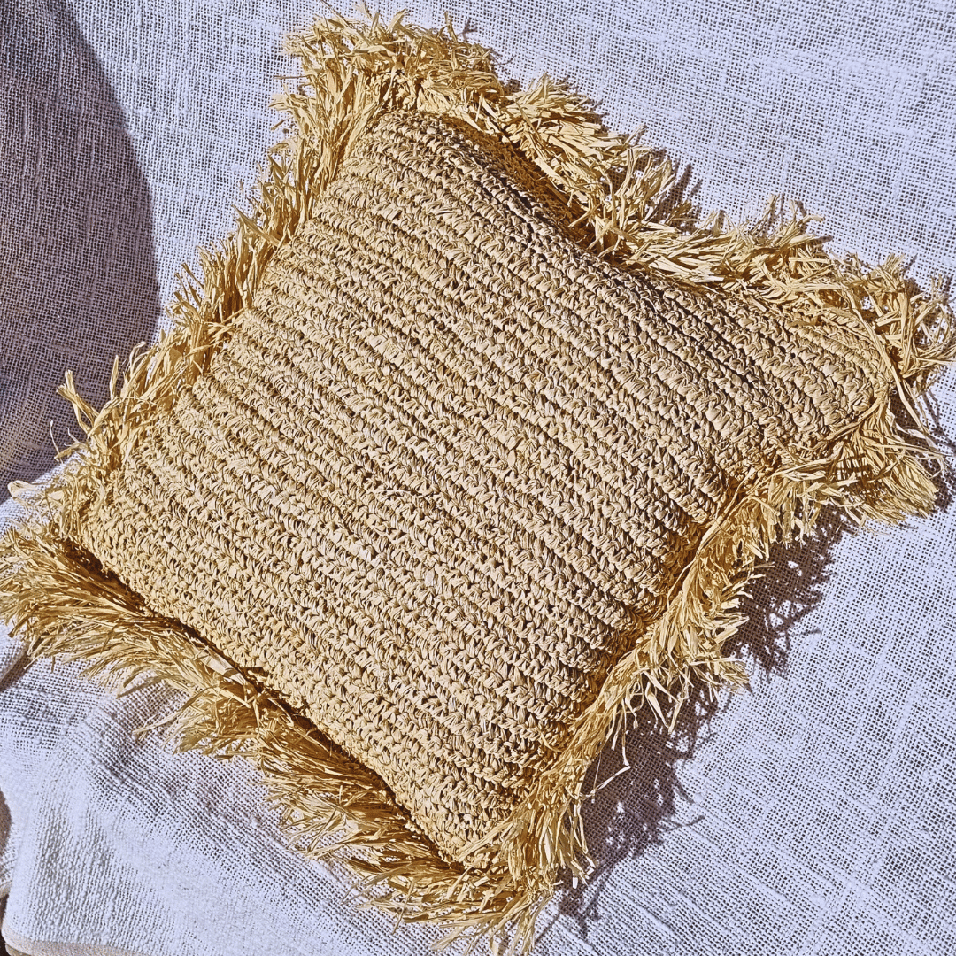 Cojín Balangan cuadrado de rafia natural estilo boho sobre sillón.
