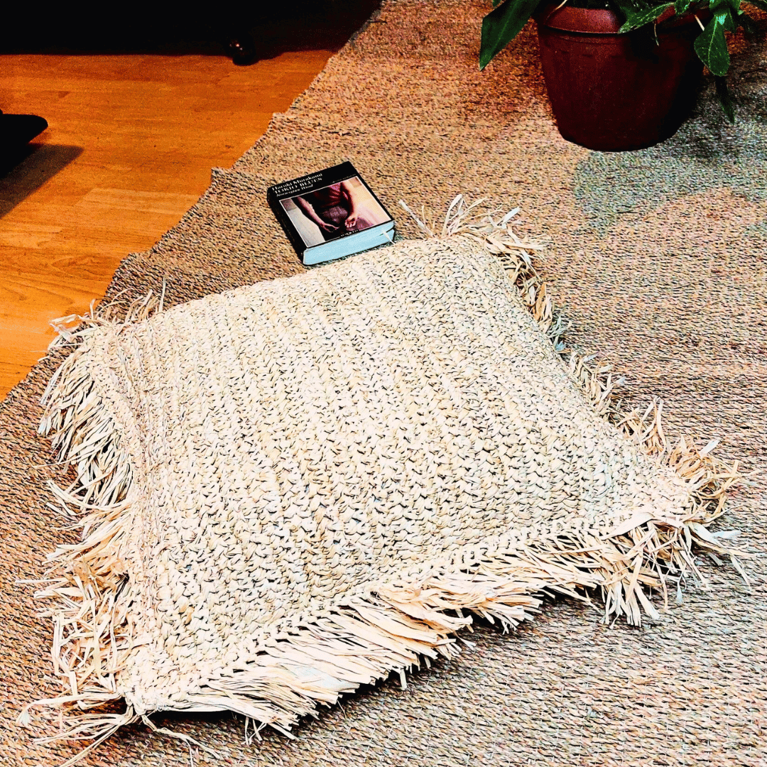 Cojín Balangan cuadrado de rafia sobre una alfombra.