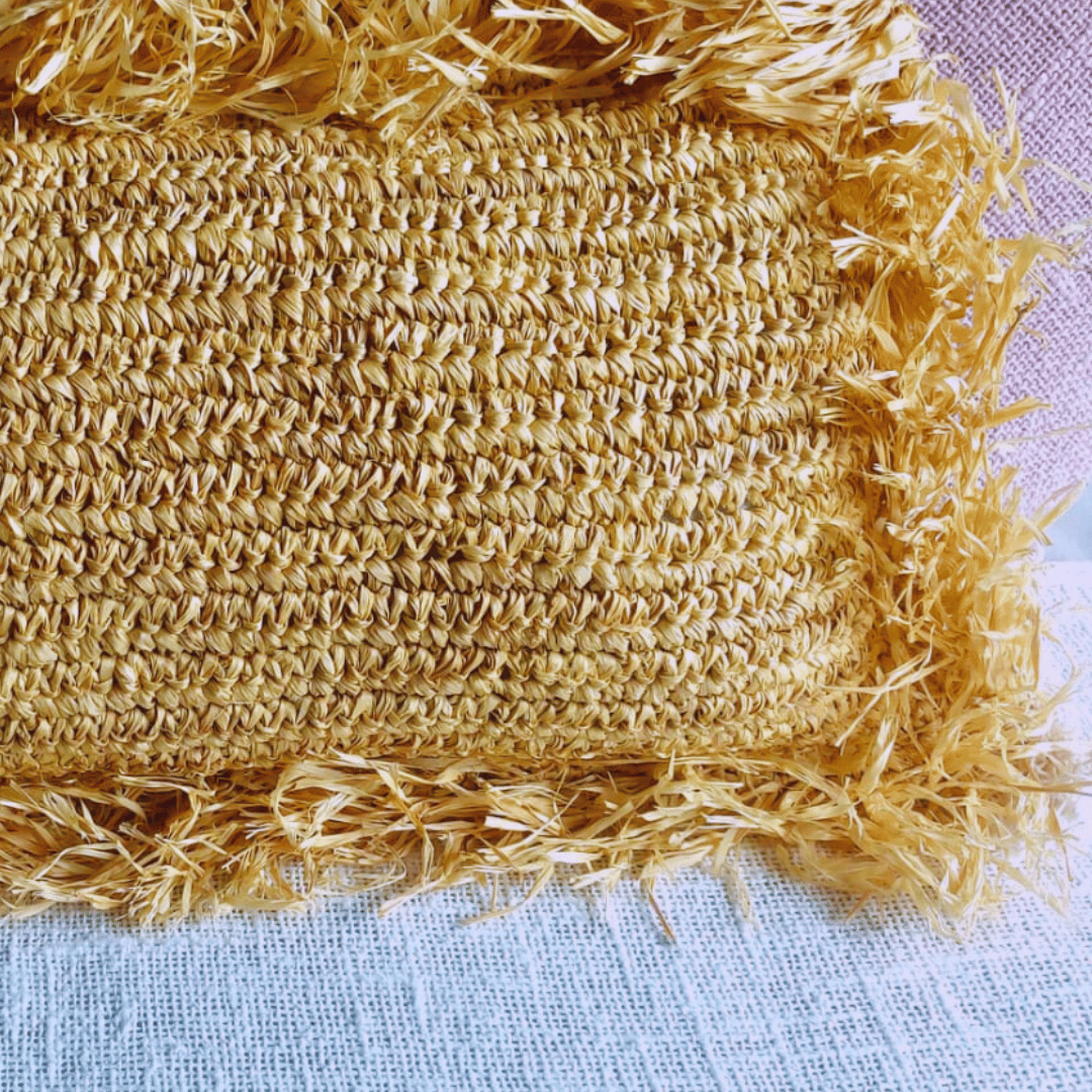 Cojín Balangan retangular de rafia natural estilo boho sobre manta.