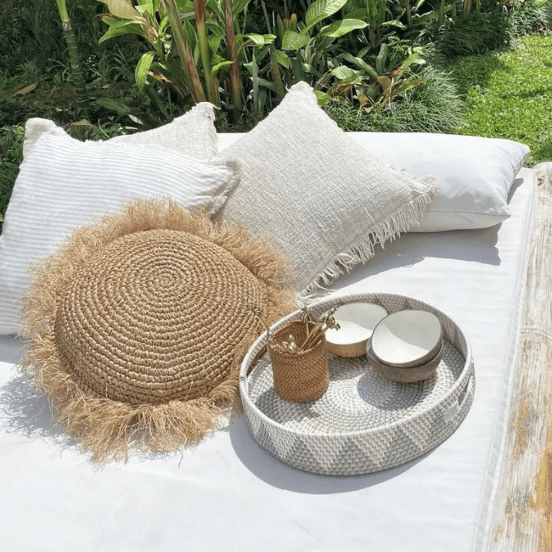 Cojín redondode rafia Balangan decorando una cama estilo playero.