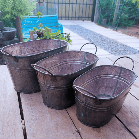 Set de tres maceteros metálicos ovalados con asas, sobre una mesa de madera