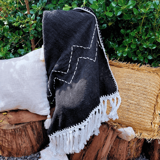 Manta Padang de algodón color negro con pompones grandes estilo boho sobre sofá.