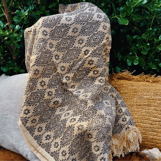 Manta Palu de algodón con diseño tribal de líneas, rombos y flecos sobre sofá."