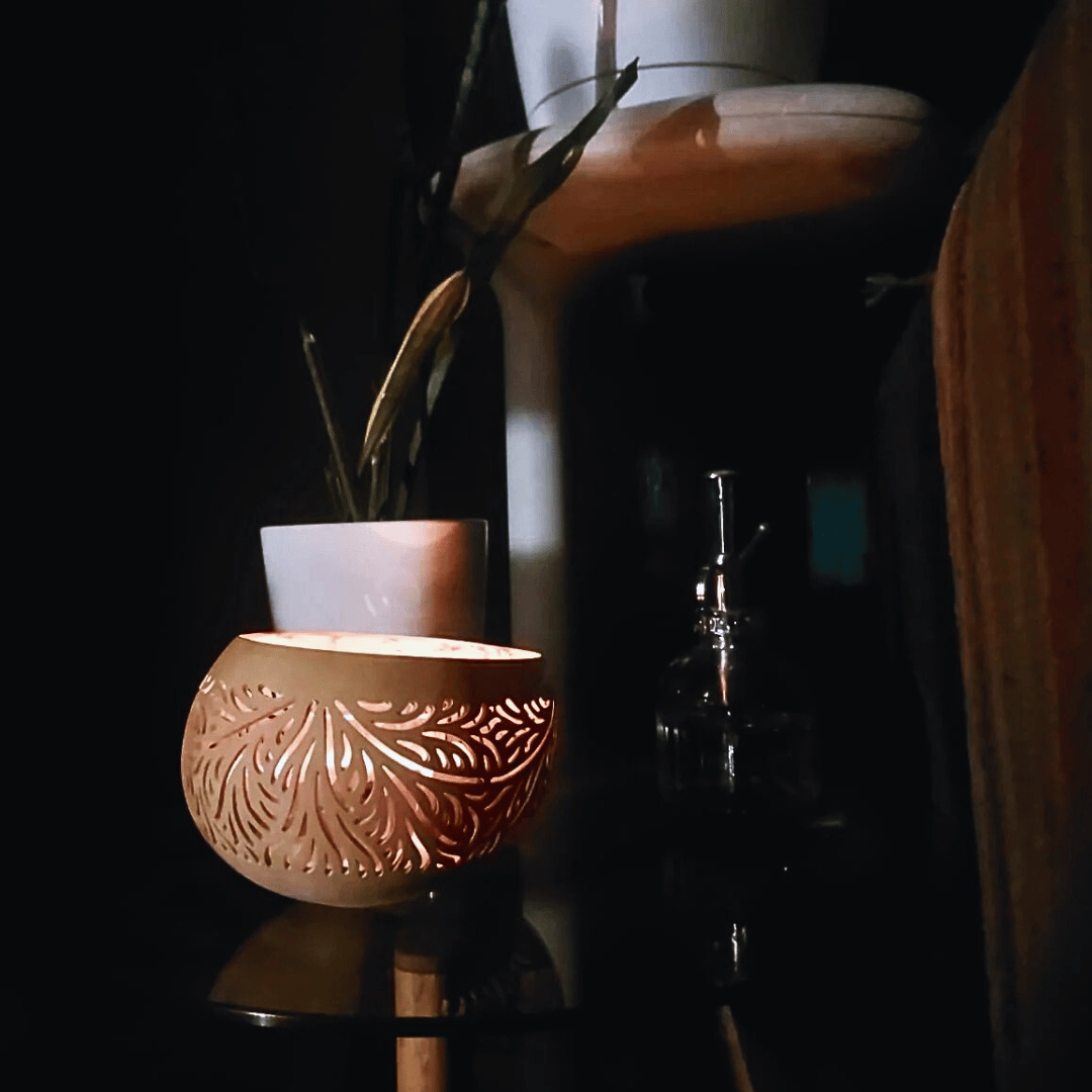 Portavela de cáscara de coco iluminando una mesa de vidrio.