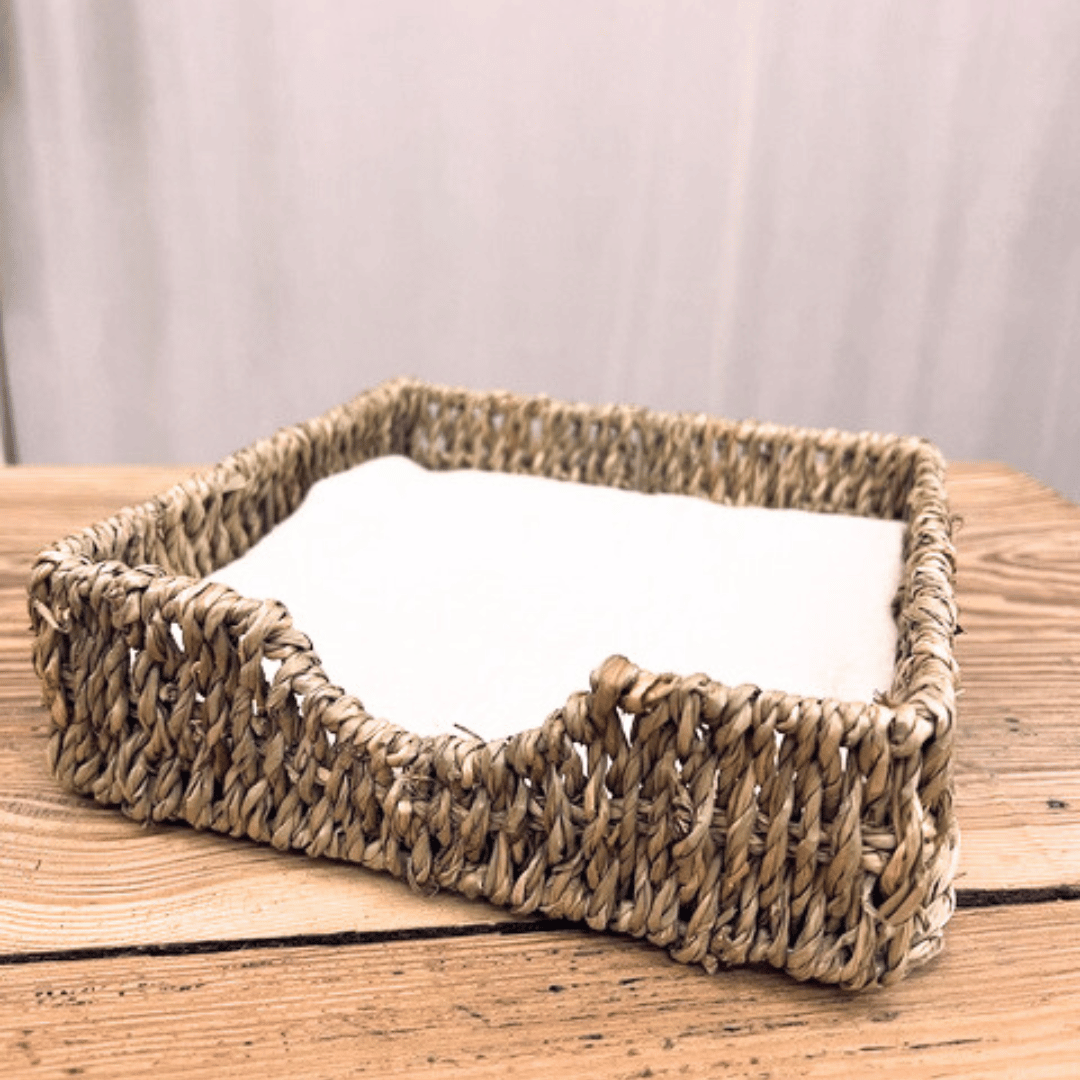 Servilletero Cu Chi de fibra natural seagrass con servilletas de tela sobre mesa de madera.